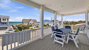 A covered outdoor area with a table and chairs, a view of the ocean, and houses in the background. - Great White Shack | 120 ft to the beach | Private Pool, Hot tub (Virginia Beach)