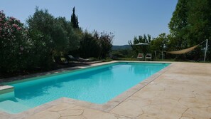 A rectangular swimming pool with a tiled edge, surrounded by a patio area with lounge chairs and a hammock. - A L'orée du Bois - Gîte (Hostun)