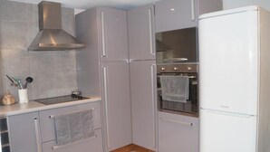 A kitchen with grey cabinets, a stainless steel range hood, a built-in oven, and a white refrigerator. - A L'orée du Bois - Gîte (Hostun)