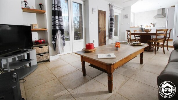 A living room with a TV, wooden table, and a dining area with chairs and a table. - A L'orée du Bois - Gîte (Hostun)