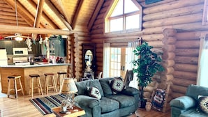A log cabin interior with a kitchen, a living area with a sofa and armchairs, a coffee table, and a dining area with stools. - Cowboy Cabin in the Mountains - Quiet Getaway (Aguilar)