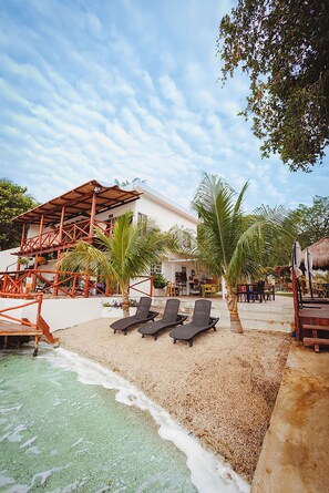 A beachside resort with a pool, lounge chairs, palm trees, and a building with a thatched roof. - El Búho Lagoon Bacalar (Bacalar)