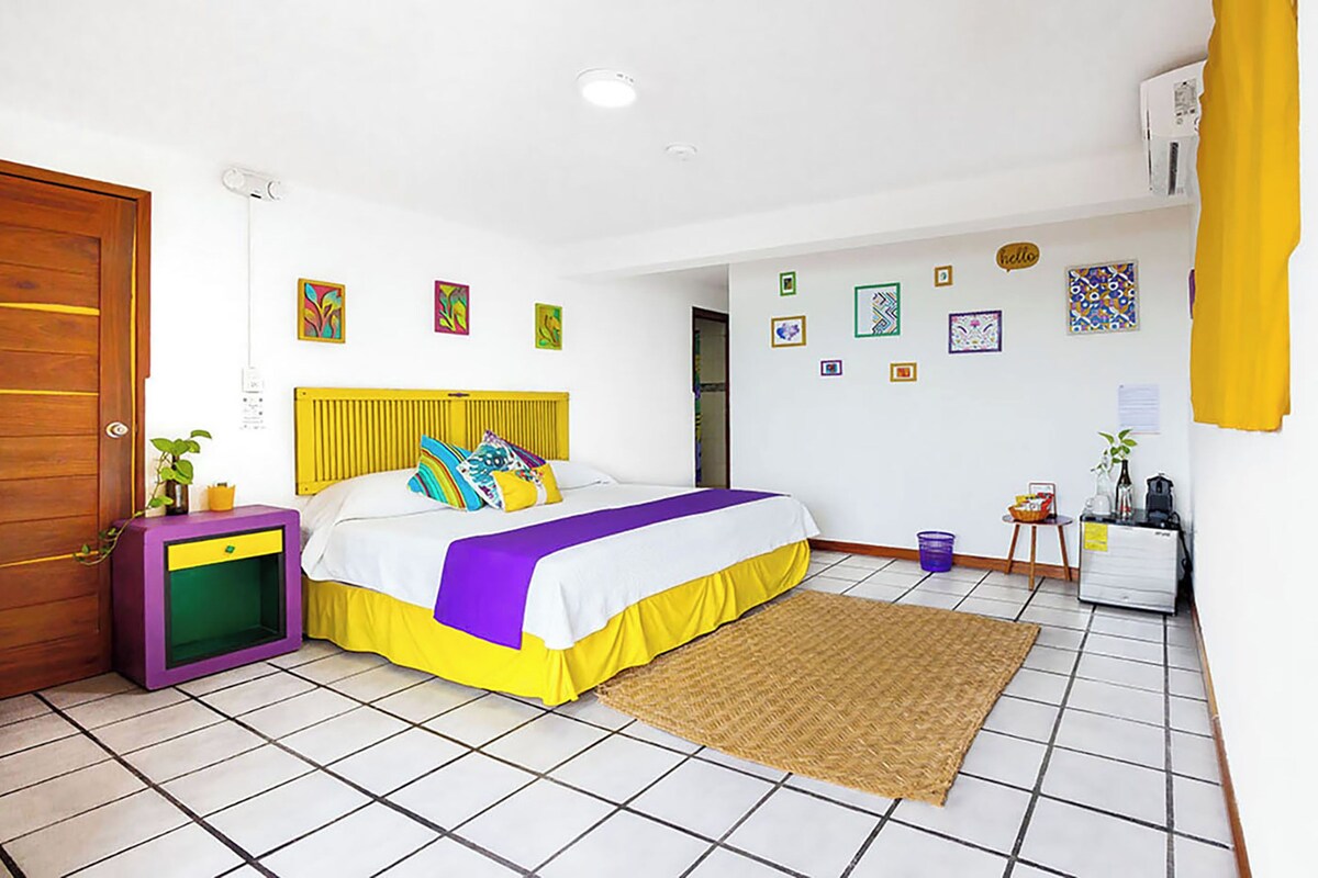 A room with a bed, a small table, a plant, and a door.