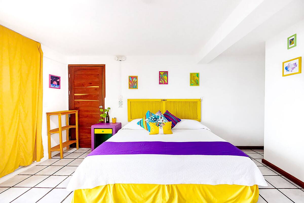 Une chambre à coucher avec un lit, une porte en bois, une petite table et un rideau jaune.