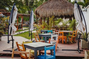 An outdoor patio with wooden tables and chairs, umbrellas, and a thatched-roof structure. - El Búho Lagoon Bacalar (Bacalar)
