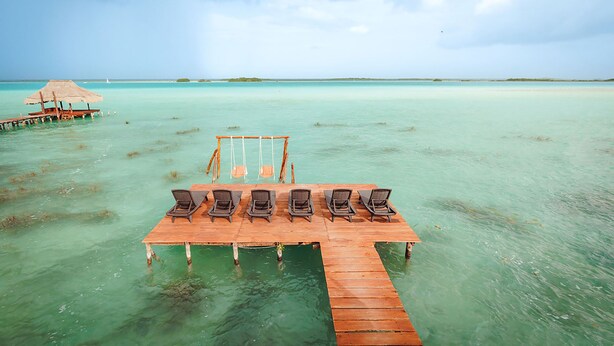 Une jetée en bois s’avançant dans des eaux turquoise, avec une hutte à toit de chaume et une rangée de chaises longues.