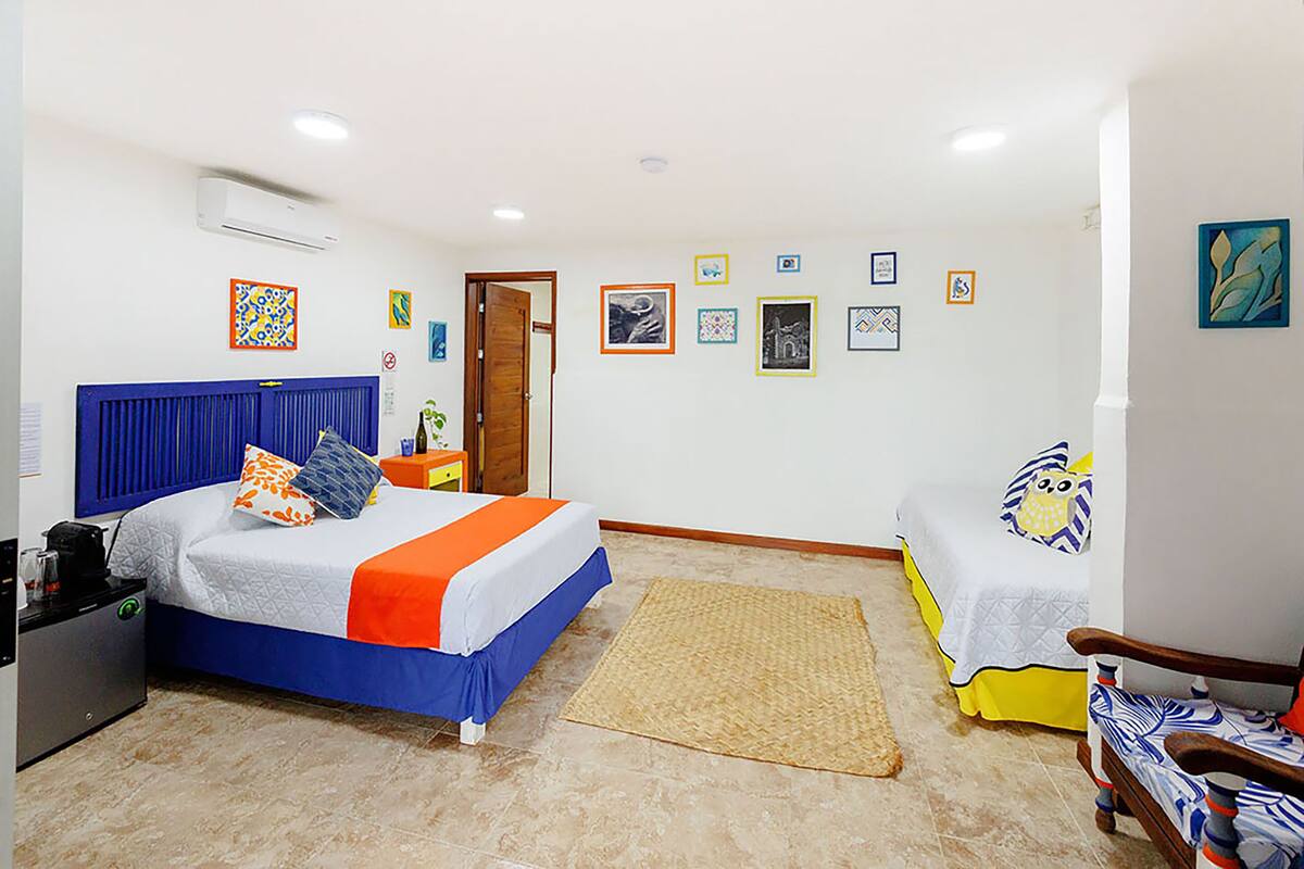 Une chambre avec deux lits, un petit bureau et une chaise. Les murs sont décorés et la pièce est équipée d’un climatiseur.