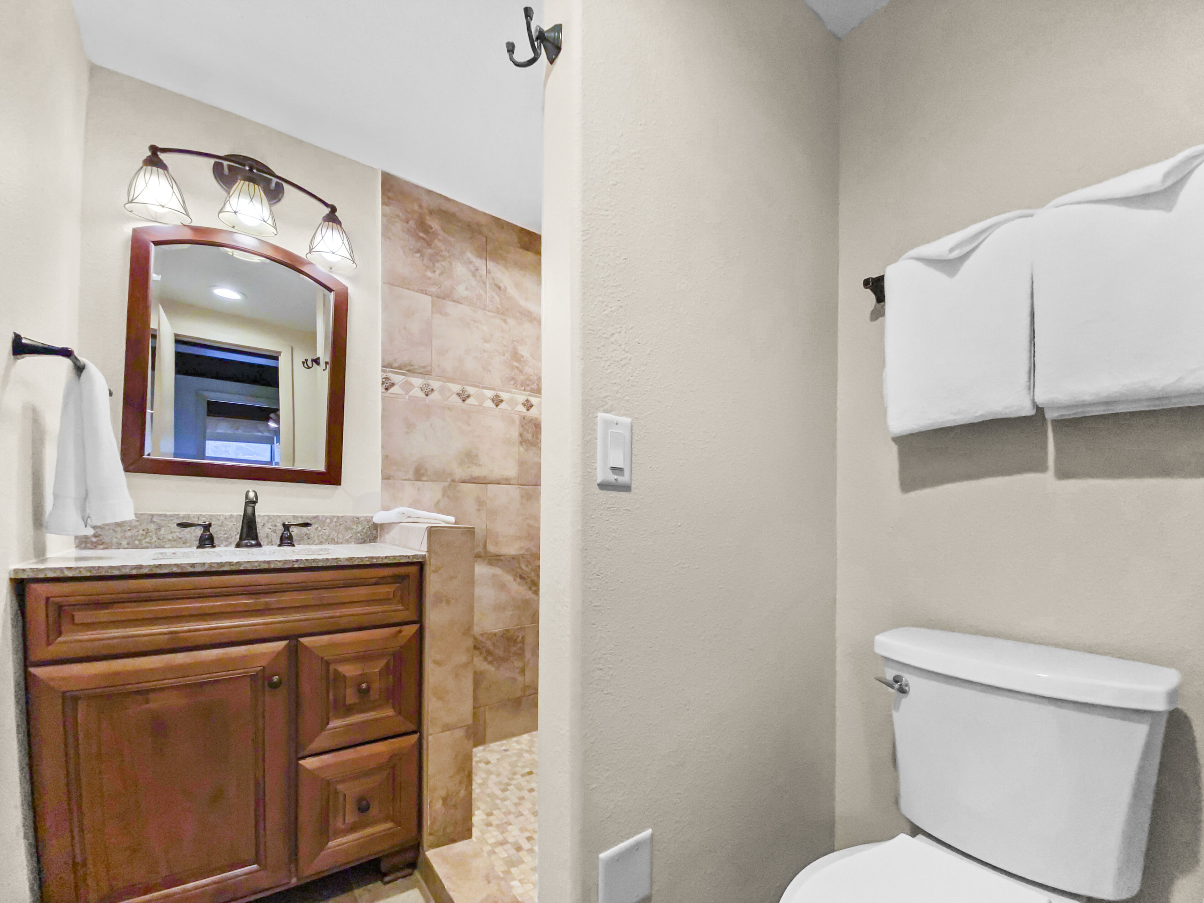 A bathroom with a wooden vanity, a mirror with lights, a toilet, and a towel rack.