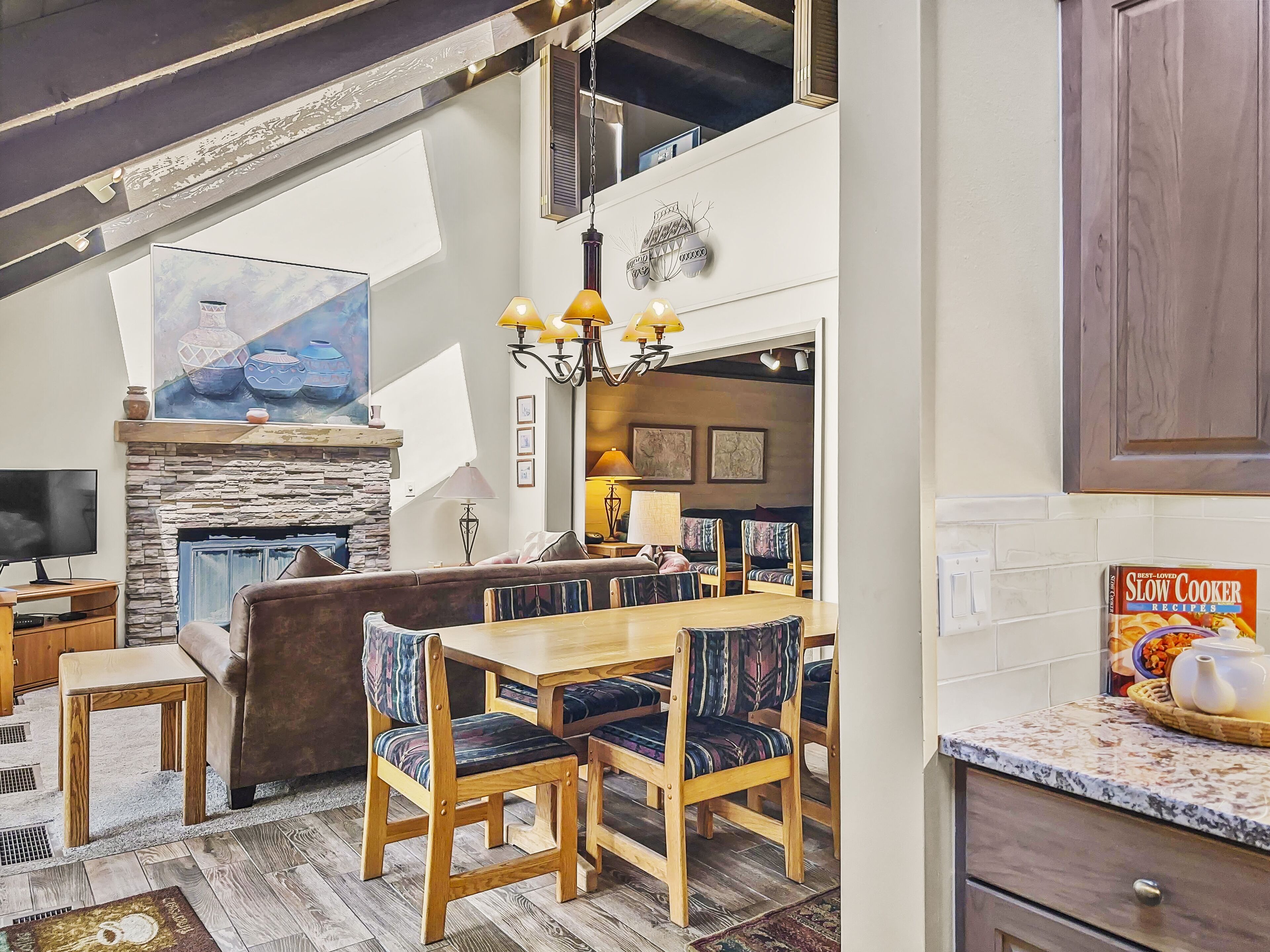A spacious dining area with a stone fireplace, wooden furniture, and a view of the upper floor.