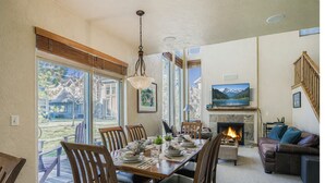 A dining area with a table set for four, a fireplace, a television, and a couch. - Trade the Office for Mountains at Foxpoint Townhouse 6180 (Park City)