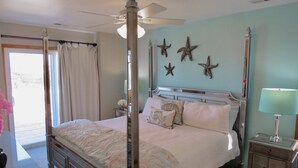 Un letto a baldacchino con tende, un comodino con una lampada, decorazioni a forma di stella marina e vista sull'esterno.