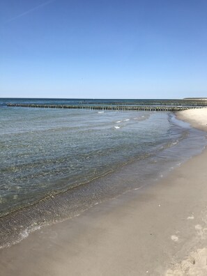 A beach with clear water, a sandy shore, and a wooden pier extending into the sea.