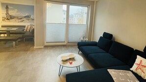 Un saló modern amb un sofà blau fosc, una taula de centre rodona i una finestra gran amb persianes.