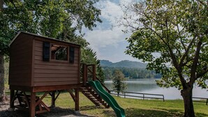 A wooden playhouse with a slide, set against a backdrop of a lake and trees. - 1BR + Loft Lake Chatuge Cabin w/ Mountain Views (Hiawassee)