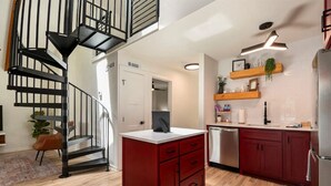 A modern kitchen with red cabinets, a stainless steel dishwasher, and a black spiral staircase. - 1BR + Loft Lake Chatuge Cabin w/ Mountain Views (Hiawassee)