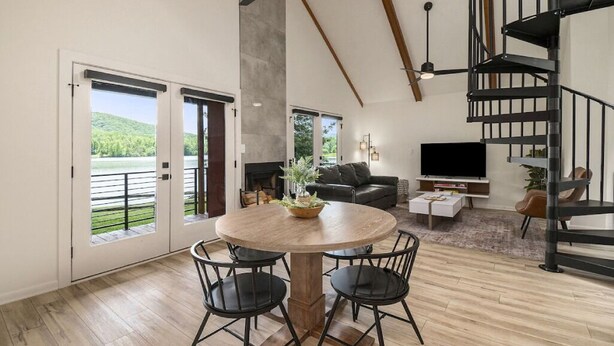 A spacious living area with a round wooden table, black chairs, a black sofa, a flat-screen TV, and a spiral staircase. - 1BR + Loft Lake Chatuge Cabin w/ Mountain Views (Hiawassee)