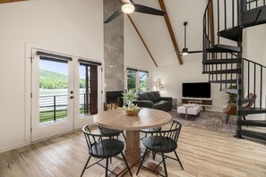 Un vaste espace de vie comprenant une table ronde en bois, des chaises noires, un canapé noir, un téléviseur à écran plat et un escalier en colimaçon.