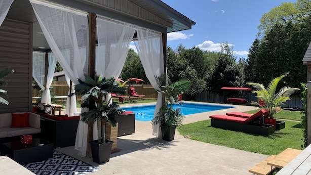 Un patio trasero con piscina, mobiliario exterior y plantas en macetas.