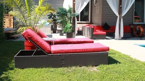 Una silla de mimbre con cojines rojos, un reposapiés rojo y una mesita con un cojín rojo.