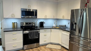 Una cocina moderna con electrodomésticos de acero inoxidable, microondas, horno y refrigerador, armarios blancos y piso de madera.