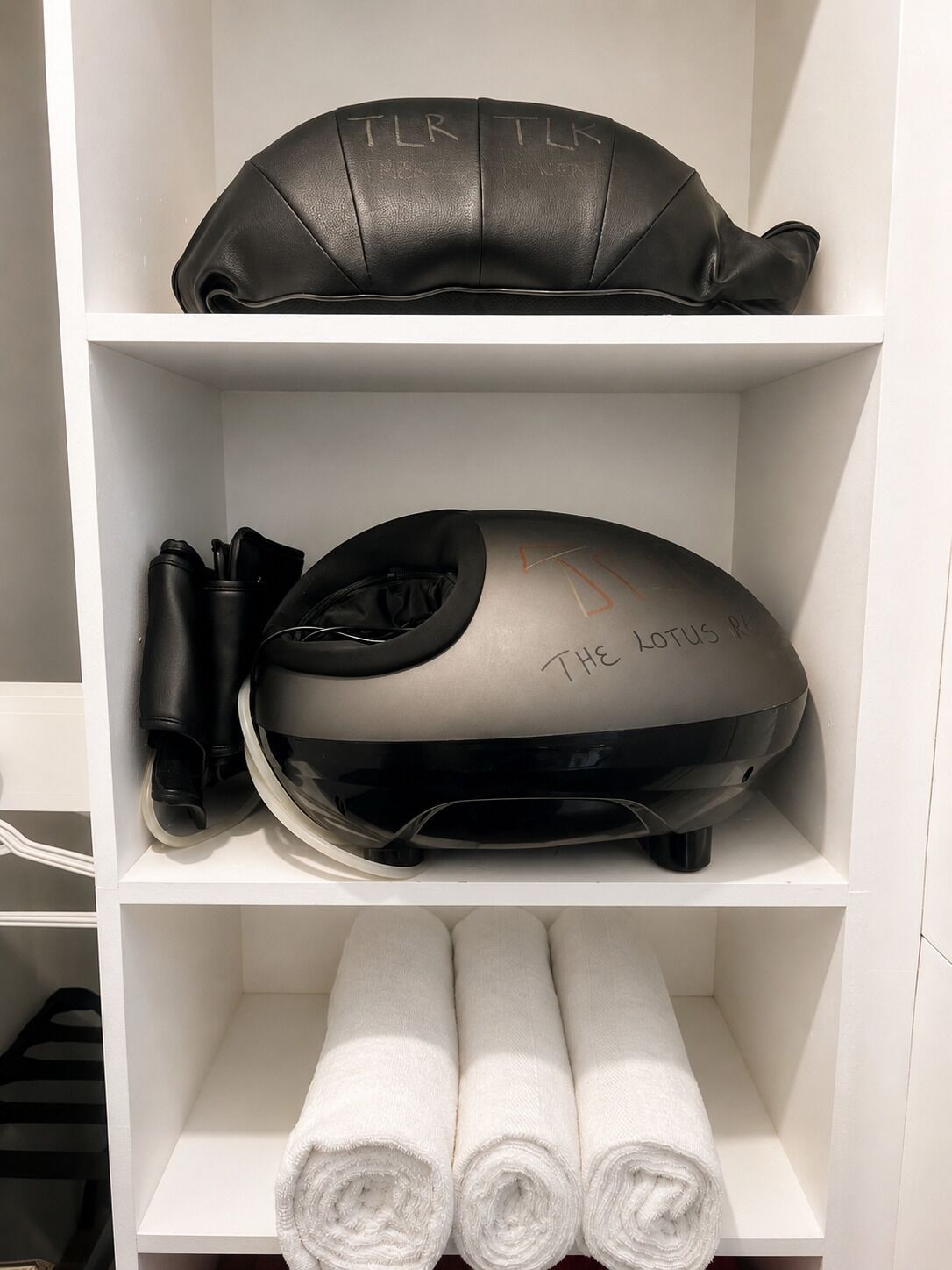 A white closet with shelves containing a black leather bag, a helmet, and rolled white towels.