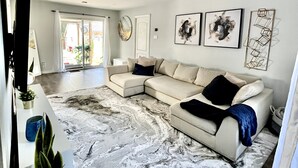 Una sala de estar moderna con un sofá seccional, una alfombra con diseño de mármol y obras de arte en las paredes.