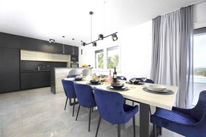 Una cucina moderna con mobili scuri, un'isola centrale e un'area pranzo con sedie blu e un tavolo chiaro.