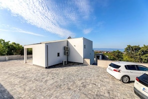Un edificio moderno con tetto piatto, condizionatori d'aria e un'area di parcheggio con due auto.
