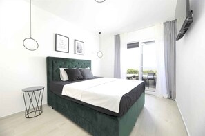 Camera da letto moderna con un letto imbottito verde, un piccolo tavolino rotondo e un'ampia finestra con tende.