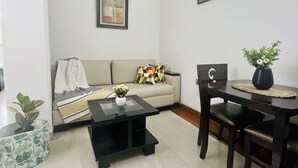 A living room with a sofa, a coffee table, a dining table with chairs, a potted plant, and an air conditioning unit. - BluO Modern Studio - Defence Colony Market (Delhi)