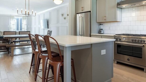 A modern kitchen with a central island, stainless steel appliances, and a dining area with a bench and chairs.