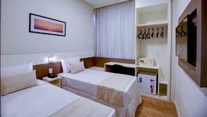 Habitación de hotel con dos camas, una mesita de noche con teléfono, perchero y un mueble de almacenamiento pequeño.