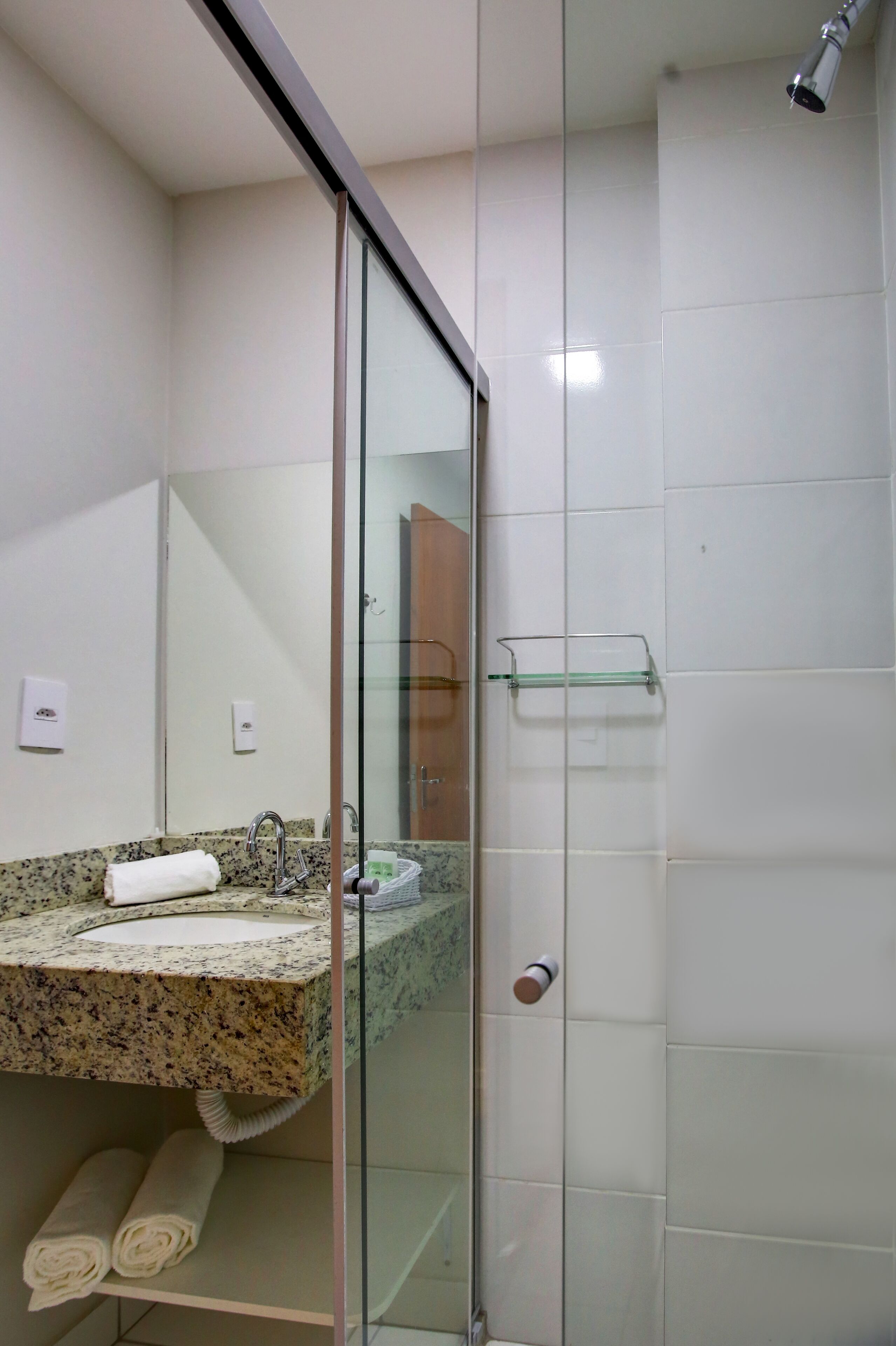 Un baño moderno con encimera de granito, cabina de ducha con paredes de vidrio y puerta de cristal.