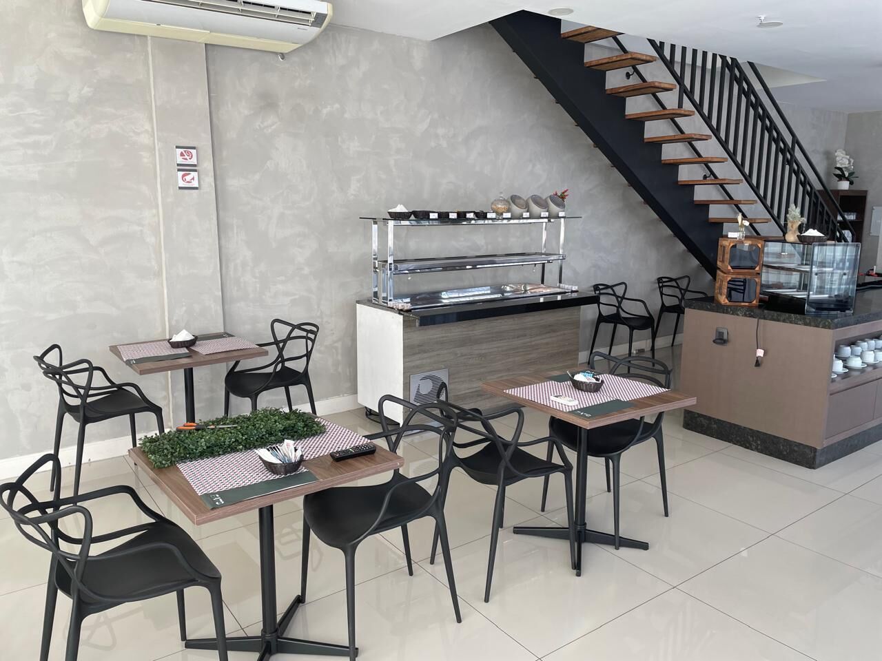 Un comedor moderno con una isla central, sillas negras y una escalera de escalones de madera.