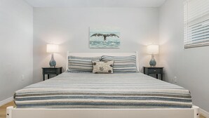 A bed with a striped bedspread, two bedside tables with lamps, a wall-mounted picture of a whale, and a window with blinds. - 2-Bedroom Condo with Waterview Balcony - Tarpon - Welcome to our stunning two-bedroom condo room with a balcony! (Matlacha)