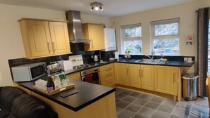 A compact kitchen with wooden cabinets, a microwave, stove, and a sink. There is a window providing natural light and a view of the outside. - The Cobbler Cottage - Loch Lomond and Arrochar Alps (Arrochar)