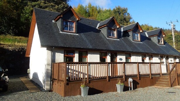 A two-story building with a sloped roof, wooden balconies, and a gravel driveway. - The Cobbler Cottage - Loch Lomond and Arrochar Alps (Arrochar)