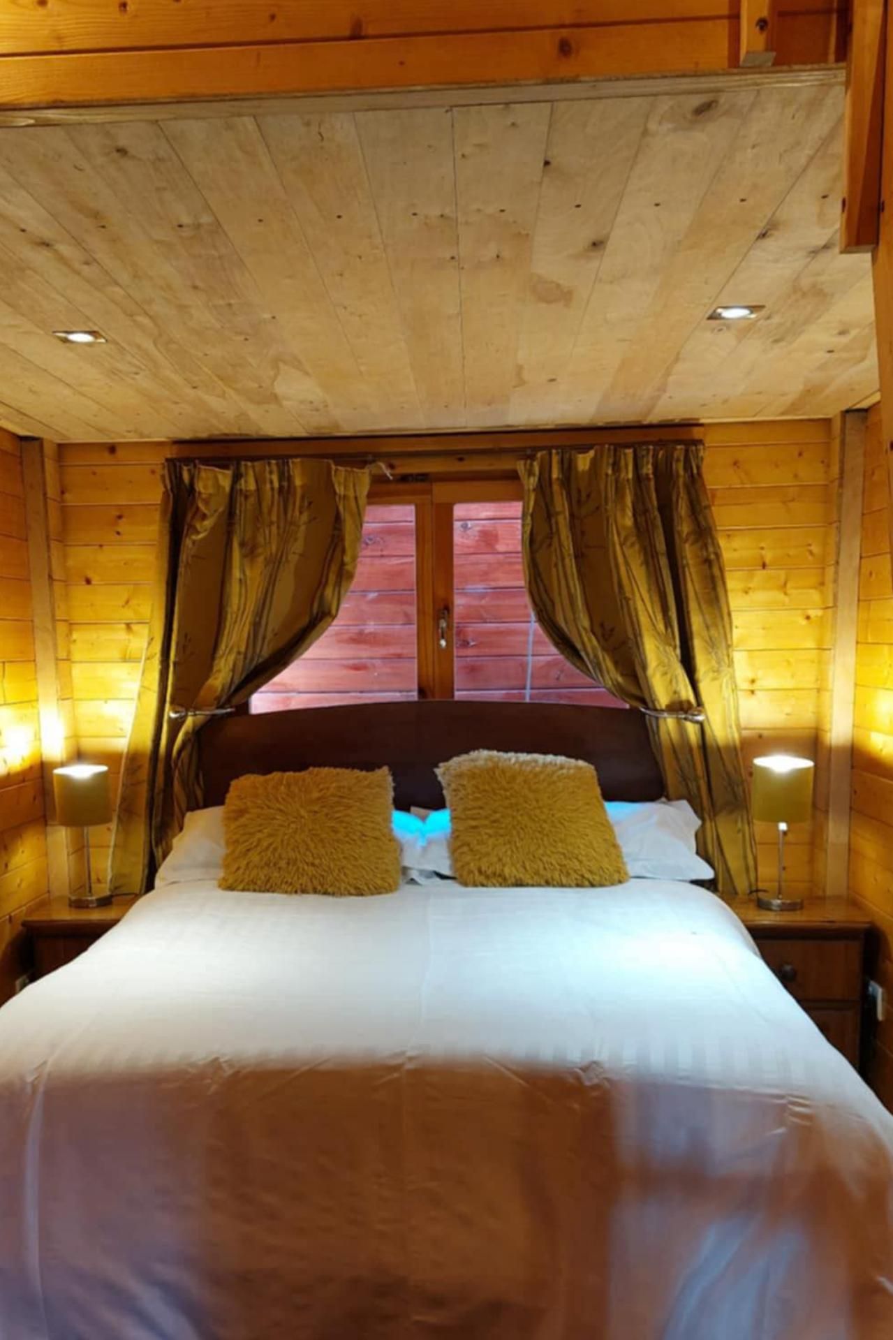 A wooden cabin bedroom with a bed, curtains, and a window.