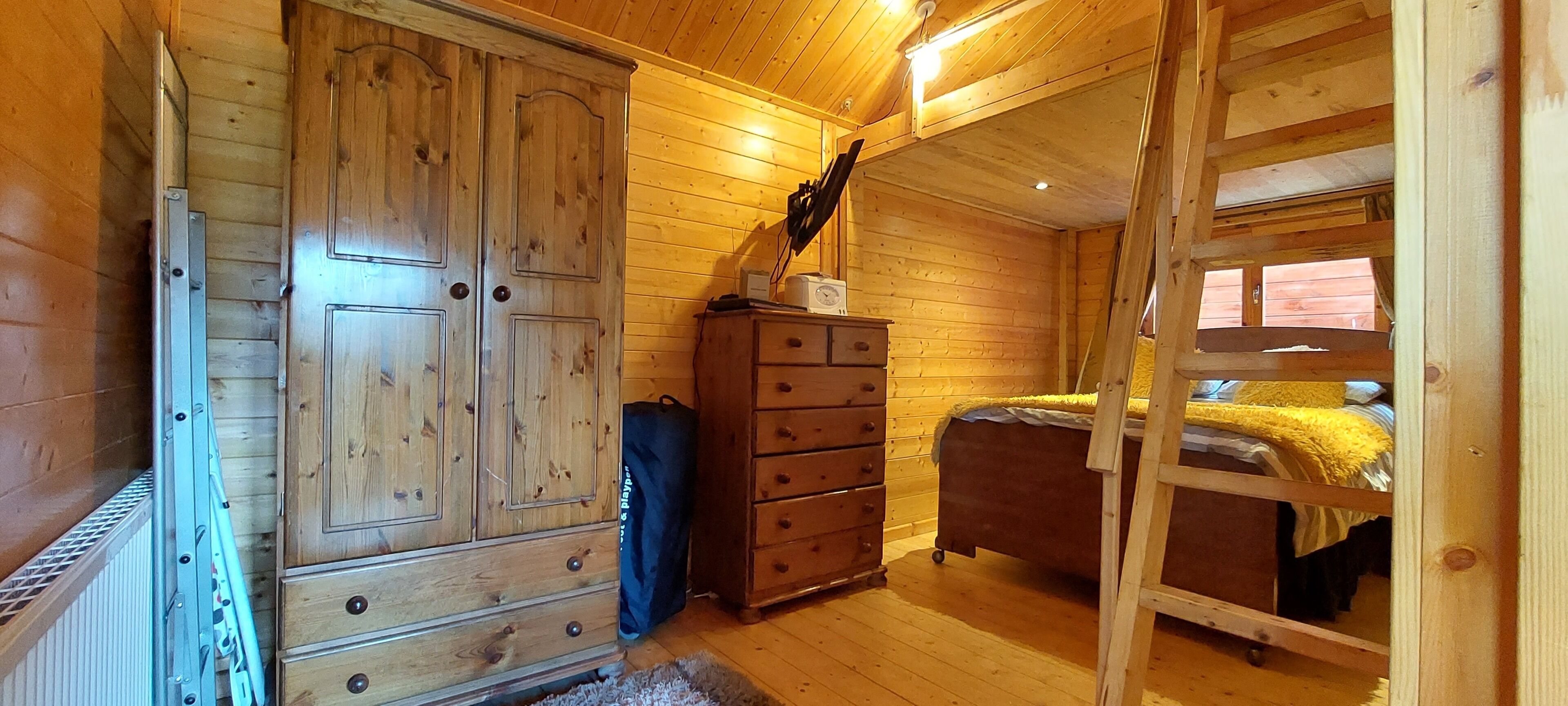 Een slaapkamer in een houten hut met een hoogslaper, een dressoir en een ladder.