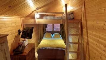 Una habitación tipo cabaña de madera con literas, una escalera, un escritorio con radio y una ventana con cortinas.