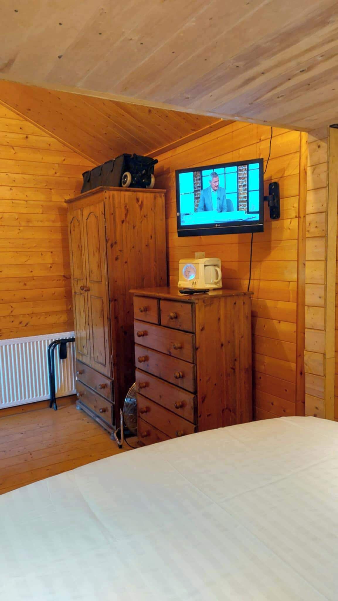 Et rum med træpaneler, et fjernsyn ophængt på væggen, en kommode med skuffer, en radiator og en seng.