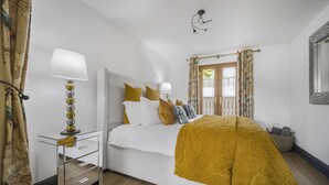A bedroom with a bed, bedside lamps, a nightstand, a window with curtains, and a mirror on the wall. - Coach House (Bridgend)