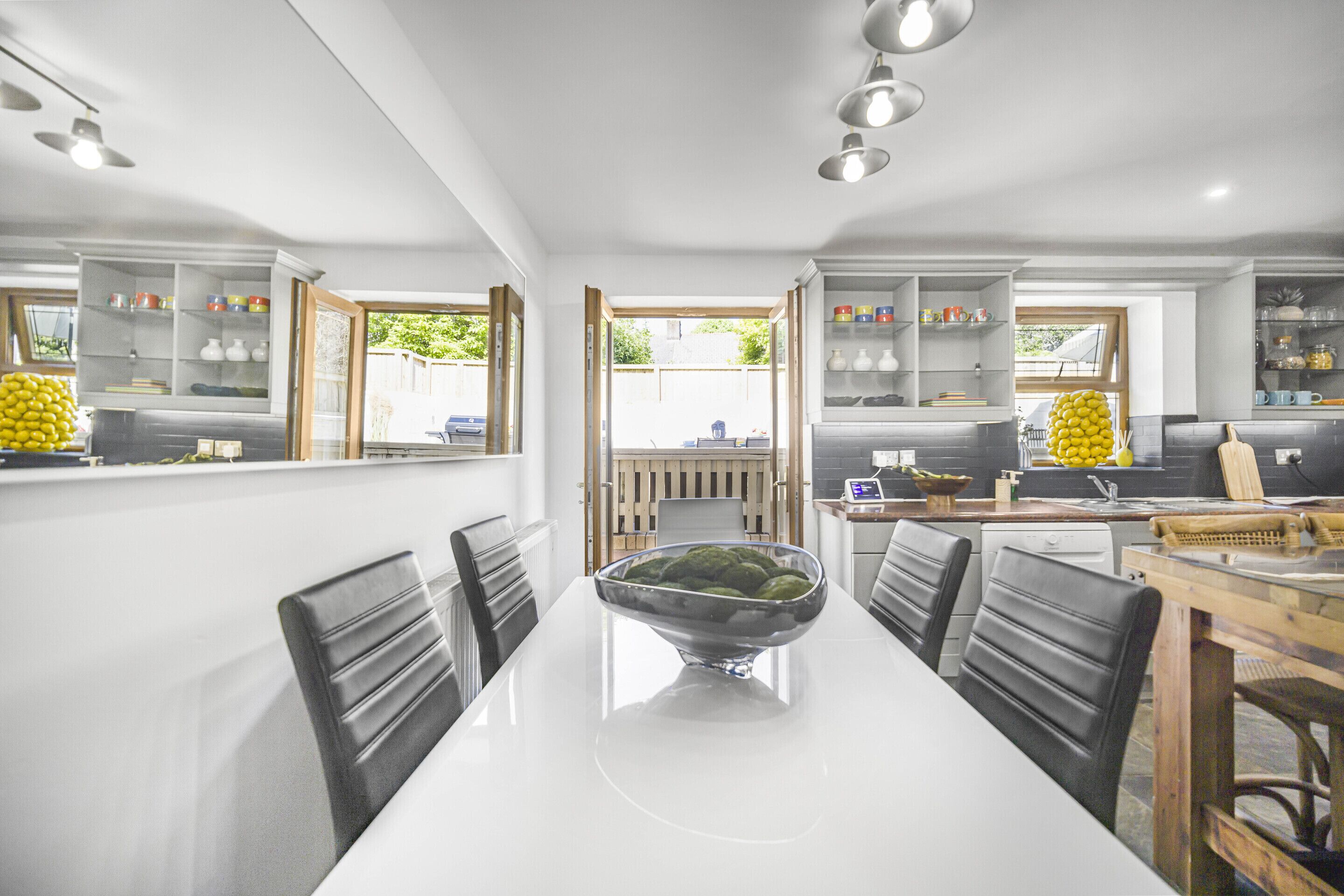 A modern kitchen with white cabinets, a central island with a bowl of fruit, and a view to the outside.