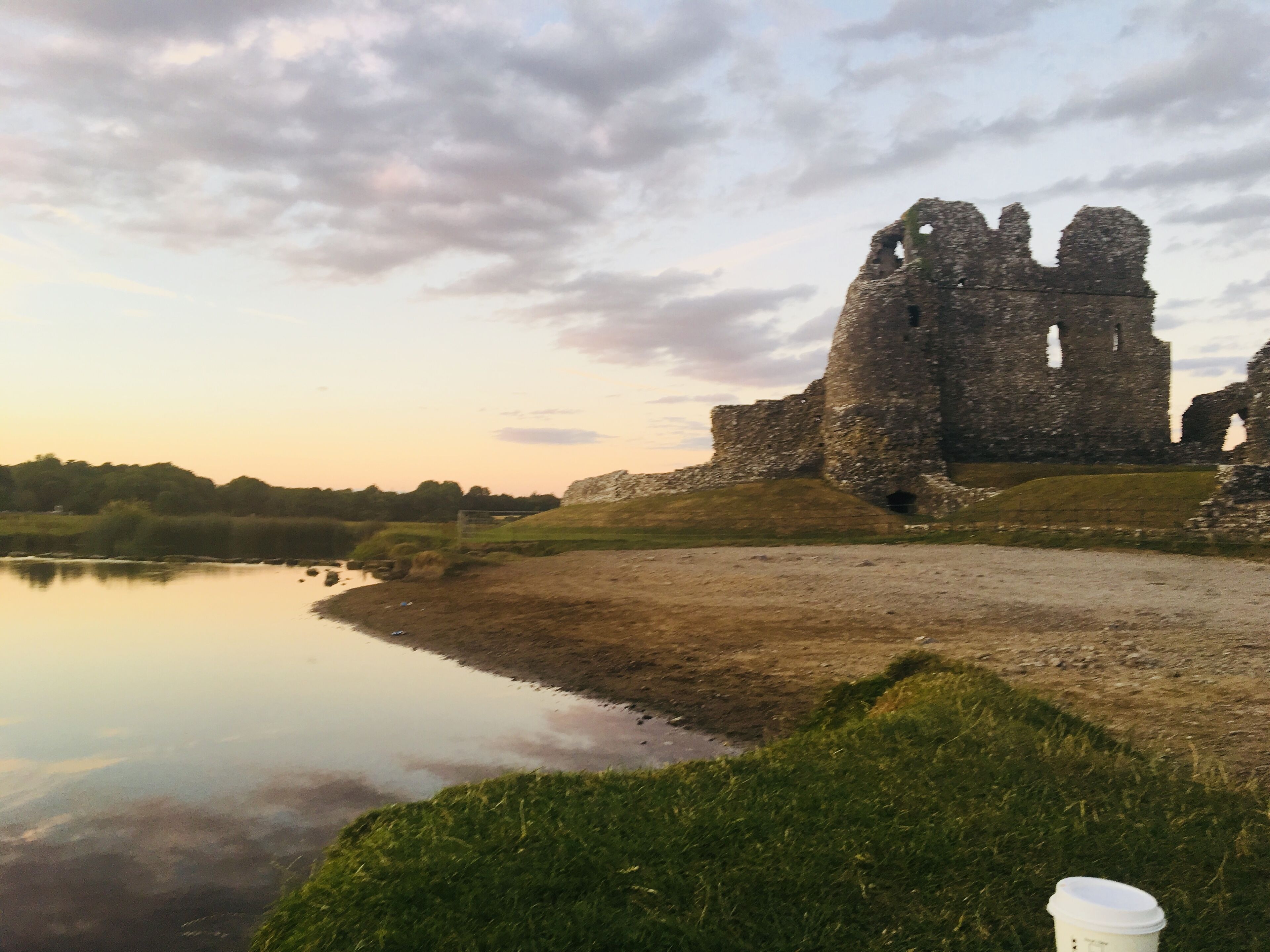 A historic stone castle with ruins, a calm lake, and grassy areas in the foreground.