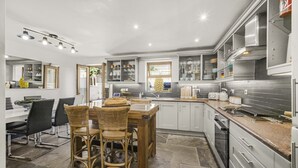 A modern kitchen with a dining area, featuring a central island, built-in appliances, and ample storage. - Coach House (Bridgend)