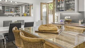 A modern kitchen with a glass-top dining table, wicker chairs, and a loaf of bread on the table. - Coach House (Bridgend)