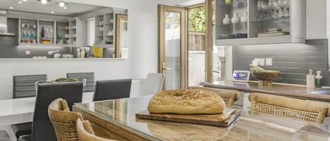 A modern kitchen with a glass-top dining table, wicker chairs, and a loaf of bread on the table.