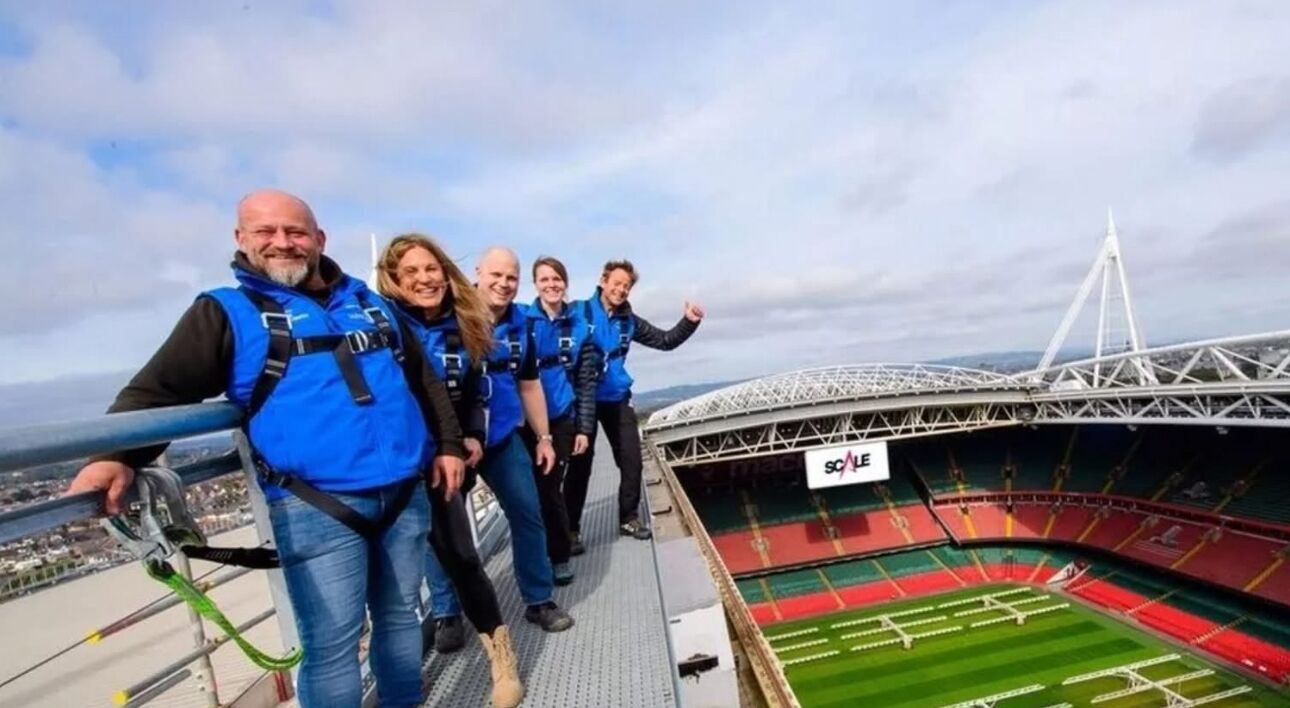 Eine Gruppe von Menschen auf einer Stadionpromenade mit Blick auf das Stadioninnere und eine Brücke im Hintergrund.