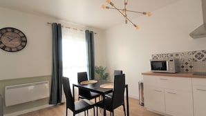 A modern kitchen with a microwave, a dining table with chairs, a clock, and a hanging light fixture. - Les Nuits Bonneuilloises Le Henson (Breteuil)