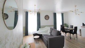 A modern living room with a sofa, dining table, chairs, and a TV. - Les Nuits Bonneuilloises Le Henson (Breteuil)